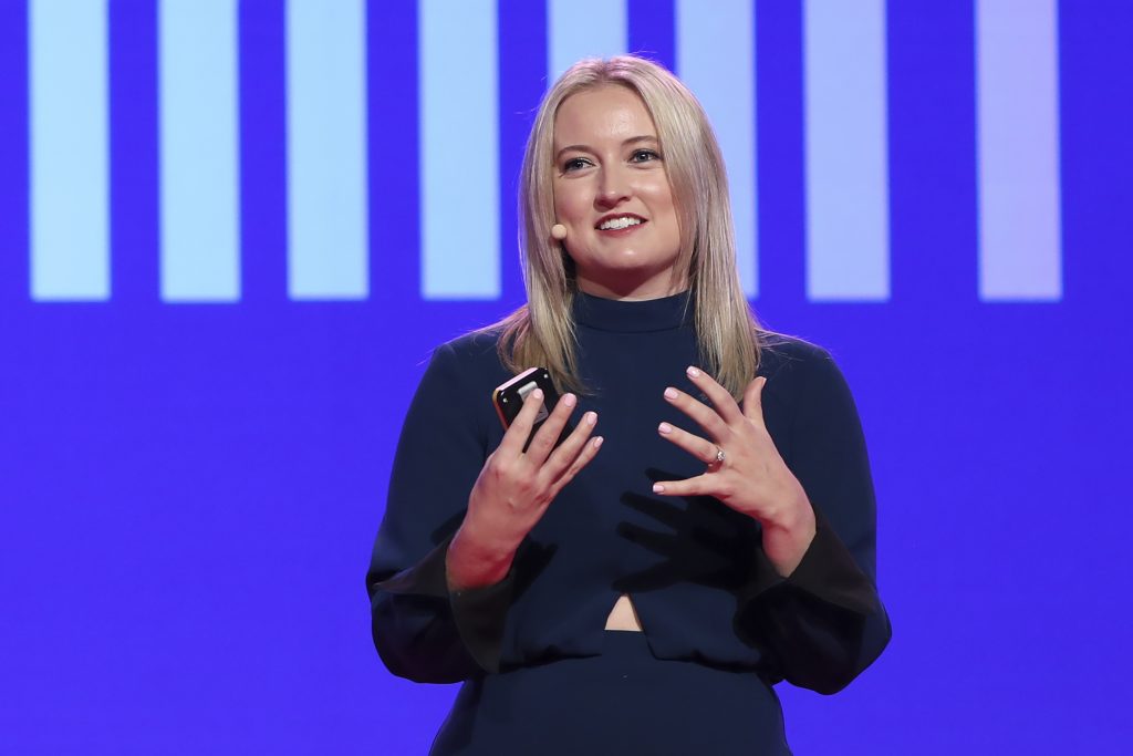 Ashley Fell speaking on stage with a striped backdrop