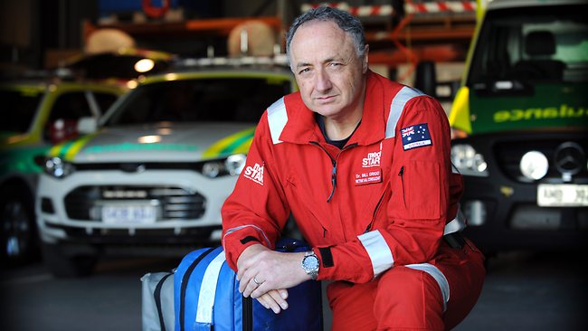 Dr Bill Griggs seated beside ambulances in a red retrieval service uniform