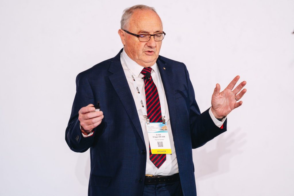 Dr Bill Griggs presenting a keynote speech with hand raised