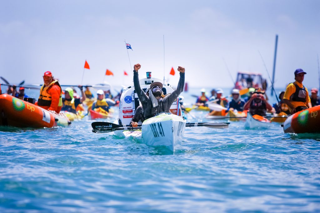 James Castrission raising his arms in celebration finishing an ocean paddling race