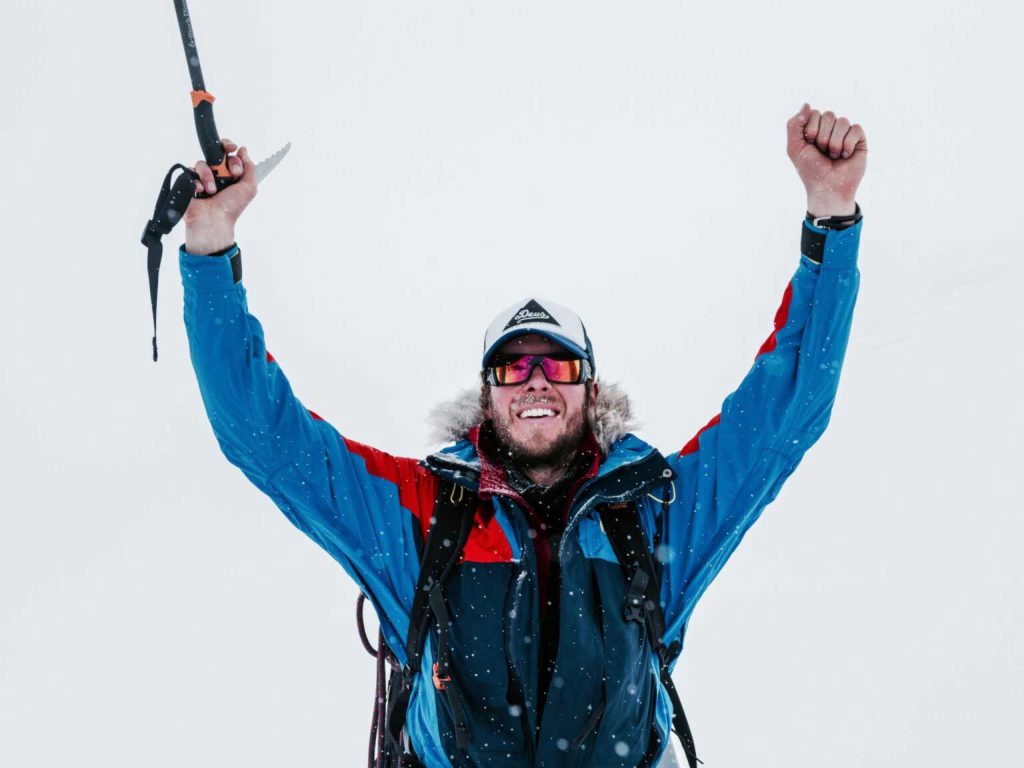 Daniel Bull raising an ice axe in celebration on a snowy mountain