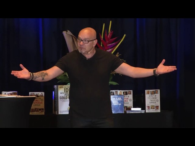Justin Herald presenting with arms outstretched in front of his books