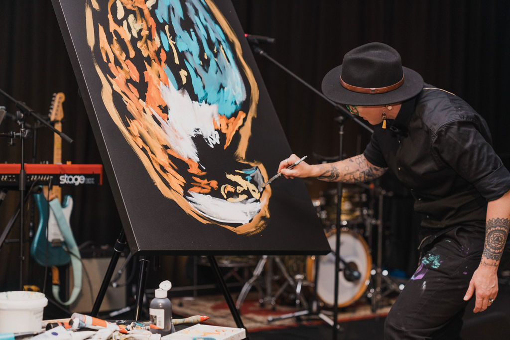 Sarah Rowan painting on an easel on stage with band equipment behind her