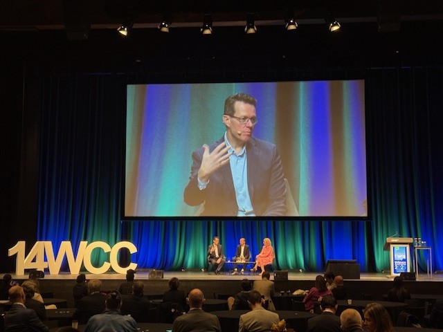 Kieren Perkins speaking on a conference stage screen